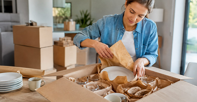 Personne emballant soigneusement de la vaisselle fragile dans un carton de déménagement avec du papier de protection